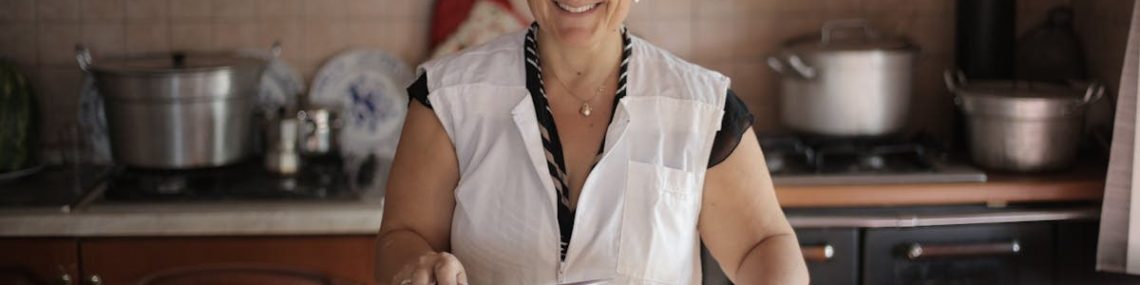 Smiling elderly woman cooking in a cozy kitchen setting, exuding warmth and hospitality.